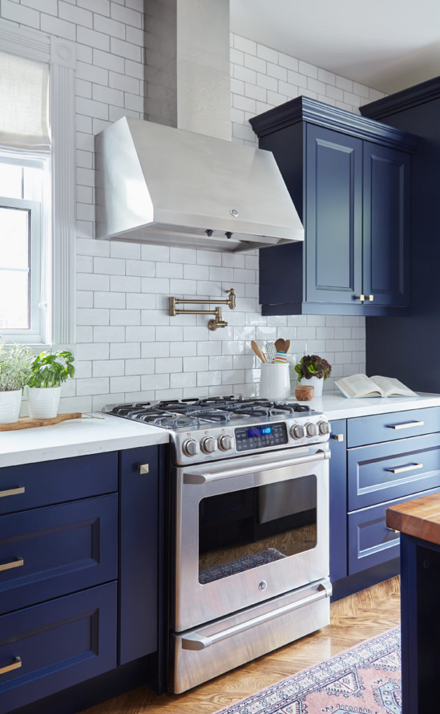 beautiful kitchen with navy blue cabinets, gold hardware, and white subway tile backsplash 