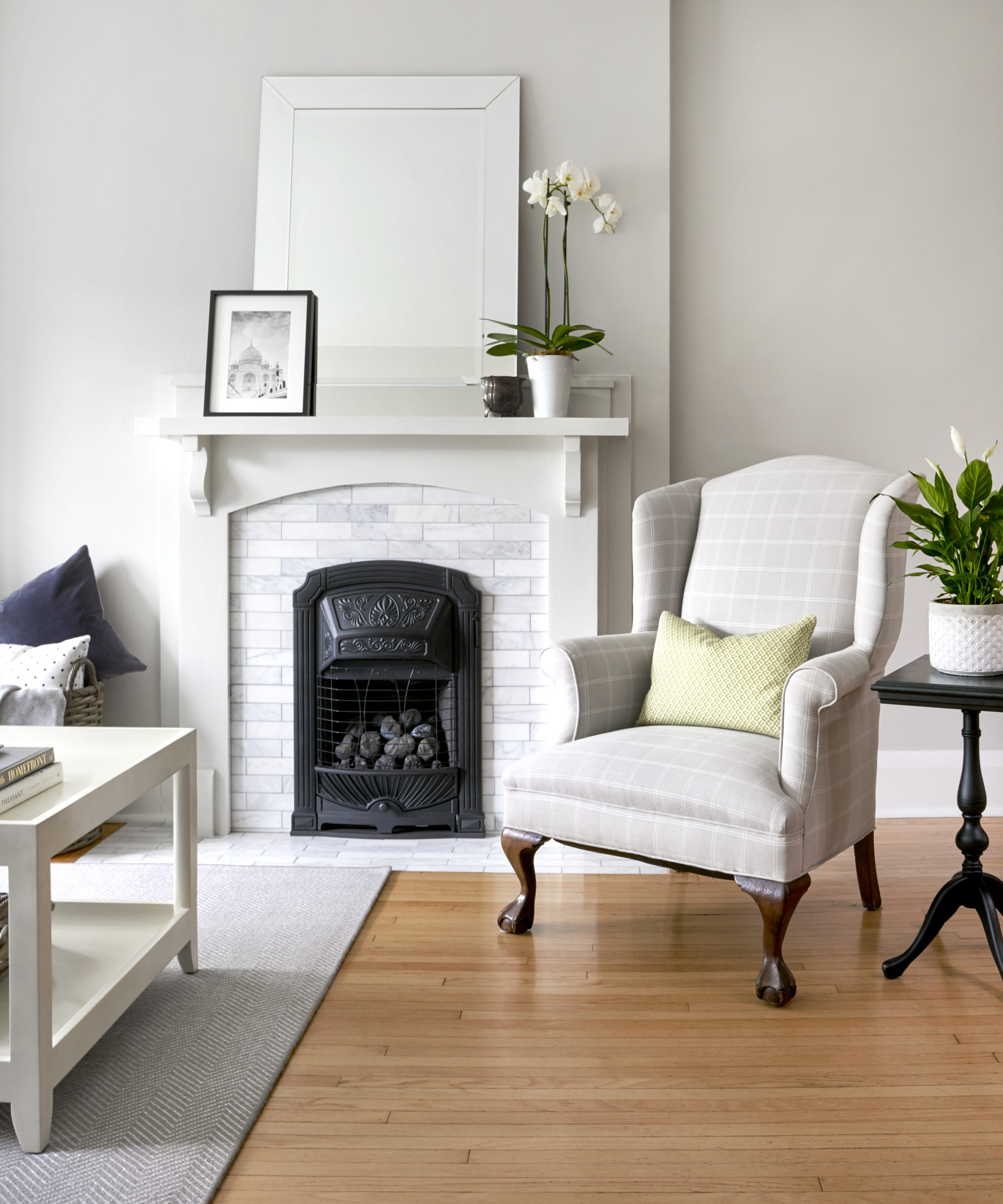 corner of a living room with a white fireplace with the mantle styled with home decor accessories, and a reupholstered wingback chair with a small green toss pillow