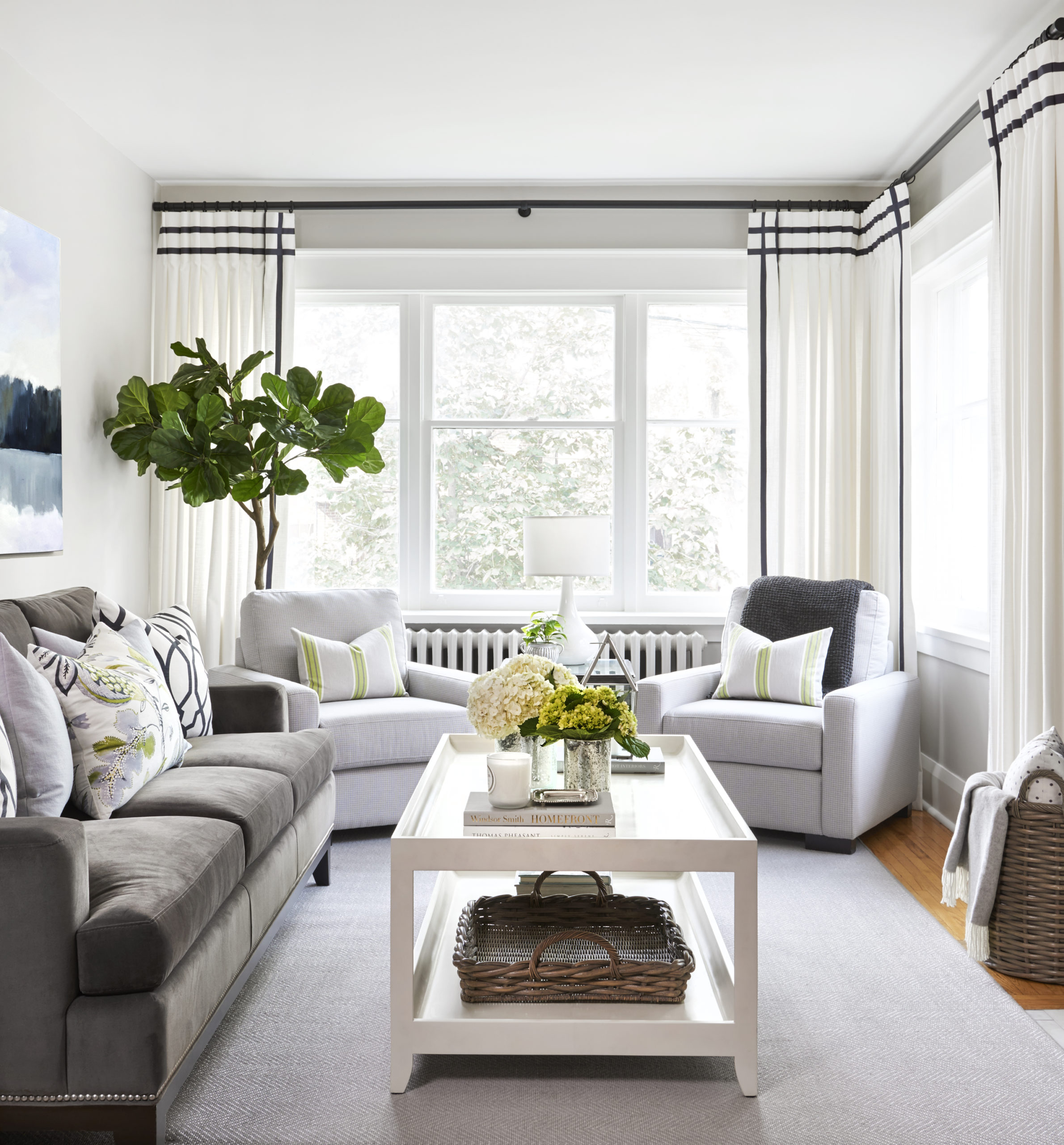 bright living room with dark grey velvet sofa, light grey armchairs, white drapery with black ribbon trim detail