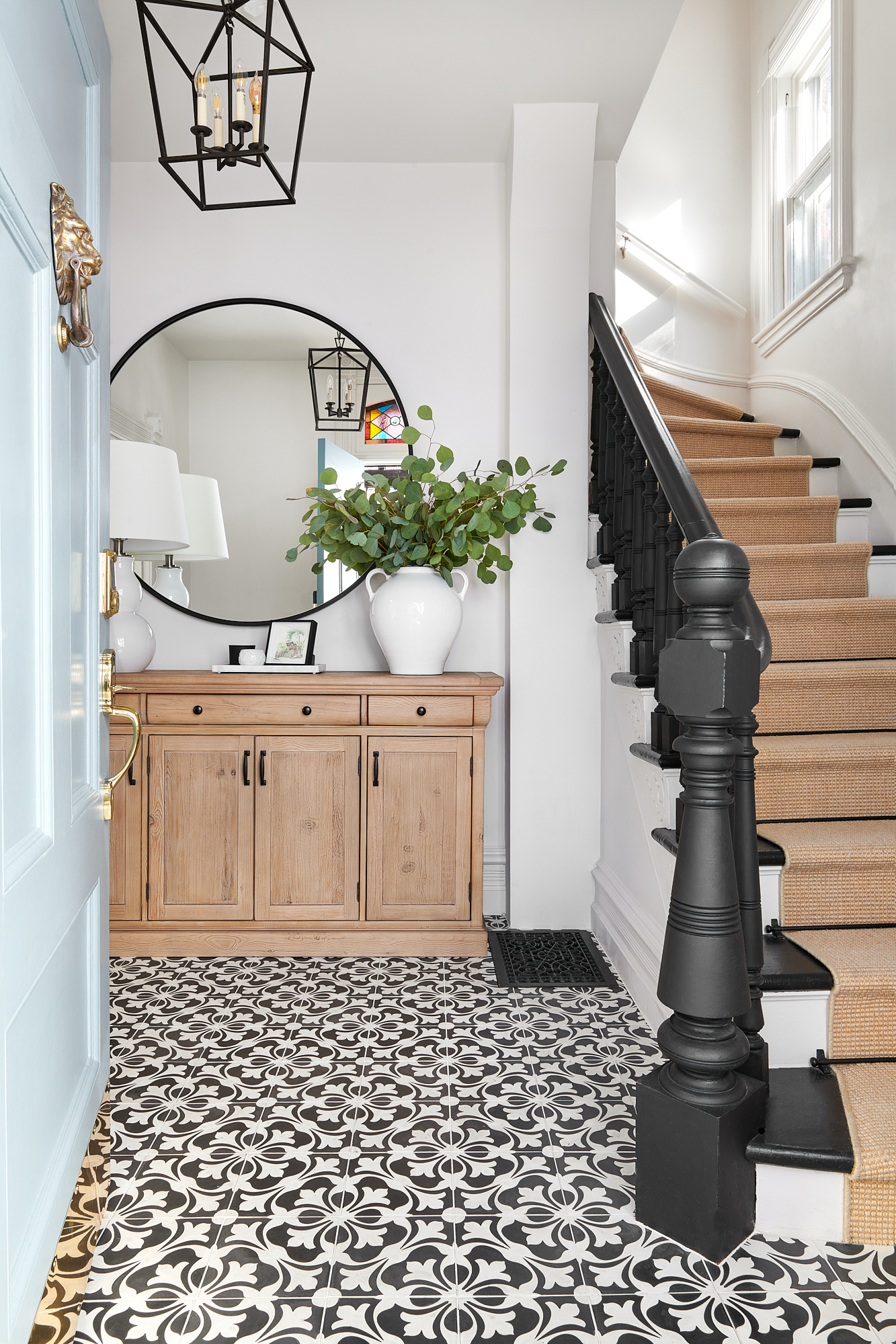 burlington foyer with black and white tile floor, wood sideboard, with white lamp and eucalyptus on top 