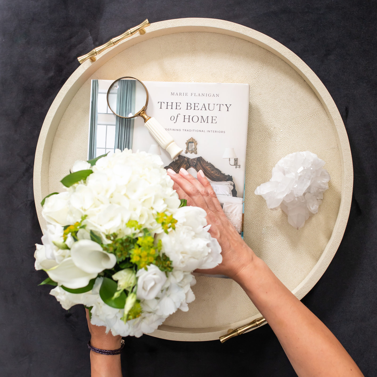 round tray layered with interior design book and someone placing flowers on top